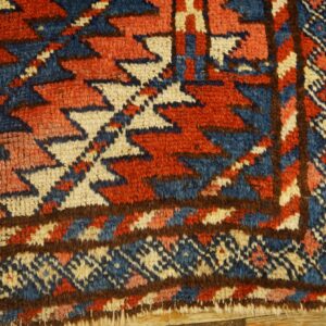 Shaggy rug detail showing geometric patterns in blue, red, cream, and brown on light wood planks.