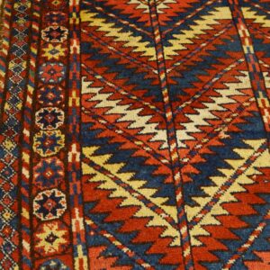 Geometric rug featuring red, blue, and cream zigzags and rosettes rests on distressed light wood planks.