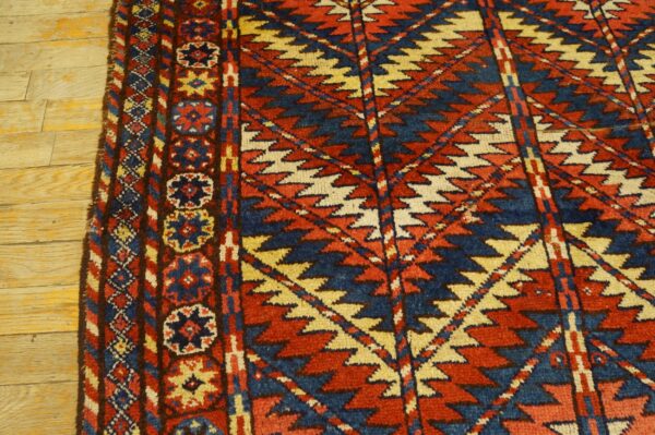 Geometric rug featuring red, blue, and cream zigzags and rosettes rests on distressed light wood planks.