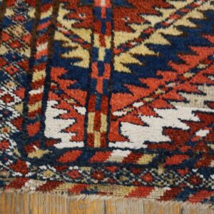 A shaggy rug corner with a stepped geometric pattern in red, blue, and white resting on wood flooring.