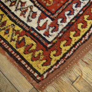Corner detail of a geometric rug with thick pile, featuring yellow and red borders on hardwood.