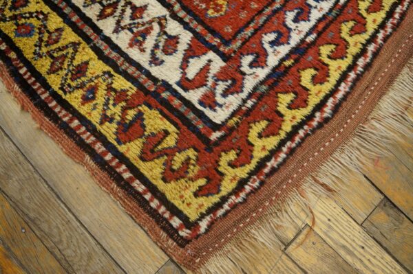 Corner detail of a geometric rug with thick pile, featuring yellow and red borders on hardwood.