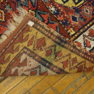 Red, blue, and yellow geometric rug folded over to show the flat woven backing on plank flooring.