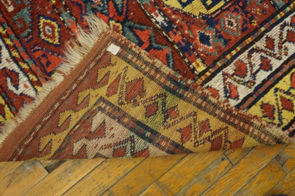 Red, blue, and yellow geometric rug folded over to show the flat woven backing on plank flooring.