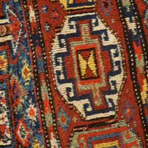 This medium pile rug detail displays intricate geometric motifs and borders using red, blue, yellow, and white colors.