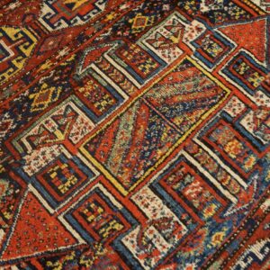 Densely patterned rug detail featuring geometric blocks of red, navy blue, yellow, and cream colors.