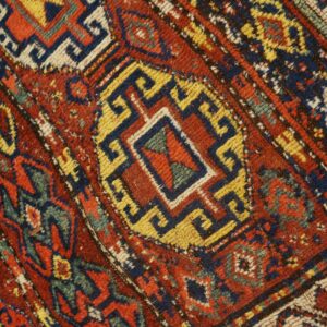 Close-up shows red pile with blue, yellow, and cream geometric stepped patterns and angular motifs.