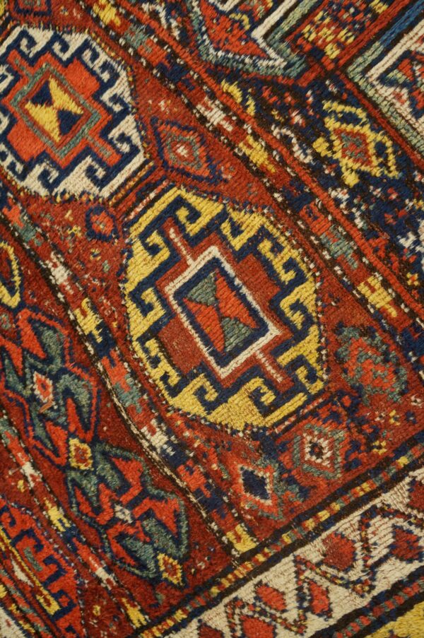 Close-up shows red pile with blue, yellow, and cream geometric stepped patterns and angular motifs.