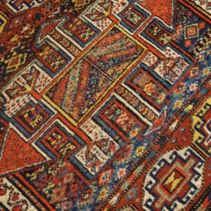 Diagonal geometric rug pattern features complex nested squares and diamonds in red, navy, and yellow.