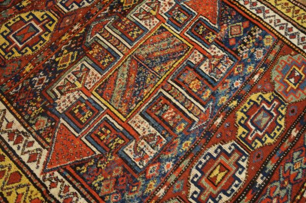 Diagonal geometric rug pattern features complex nested squares and diamonds in red, navy, and yellow.