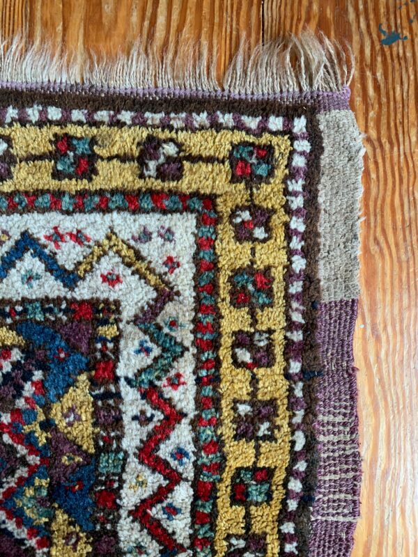 High-pile rug fragment in yellow, cream, blue, and red geometric patterns on natural wood floor.