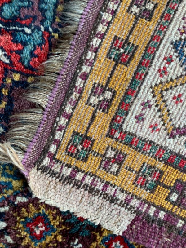 Detail of a yellow, cream, and purple geometric rug border overlapping a dense, dark red and blue floral rug.
