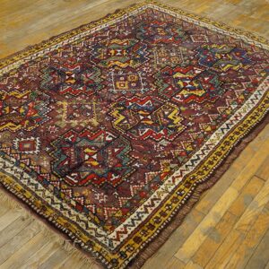 Geometric low pile rug in red, yellow, blue, and green rests on a distressed plank wood floor.