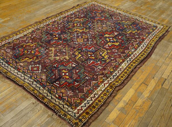 Geometric low pile rug in red, yellow, blue, and green rests on a distressed plank wood floor.