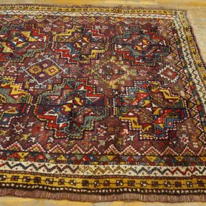 A richly colored rug with tribal geometric patterns in maroon, blue, and gold on wood flooring.