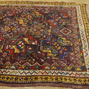 Geometric tribal rug in deep maroon, red, yellow, and blue is displayed on light hardwood.