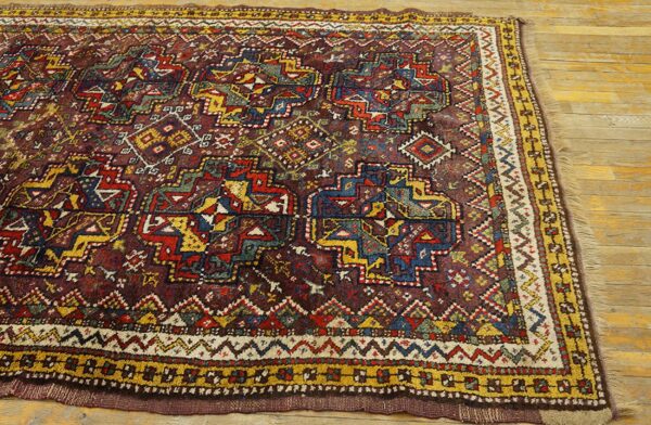 Geometric tribal rug in deep maroon, red, yellow, and blue is displayed on light hardwood.