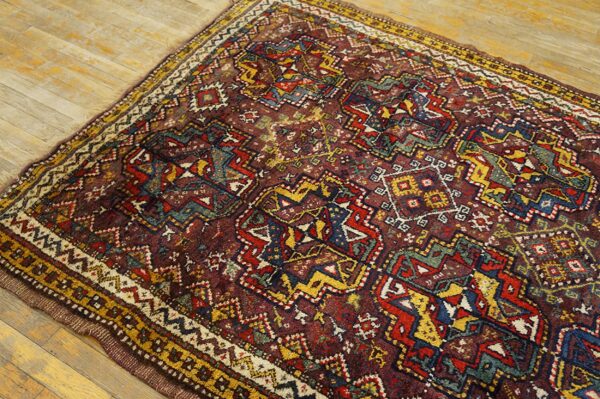Intricate geometric rug in maroon, gold, blue, and red lies on light wood plank flooring.