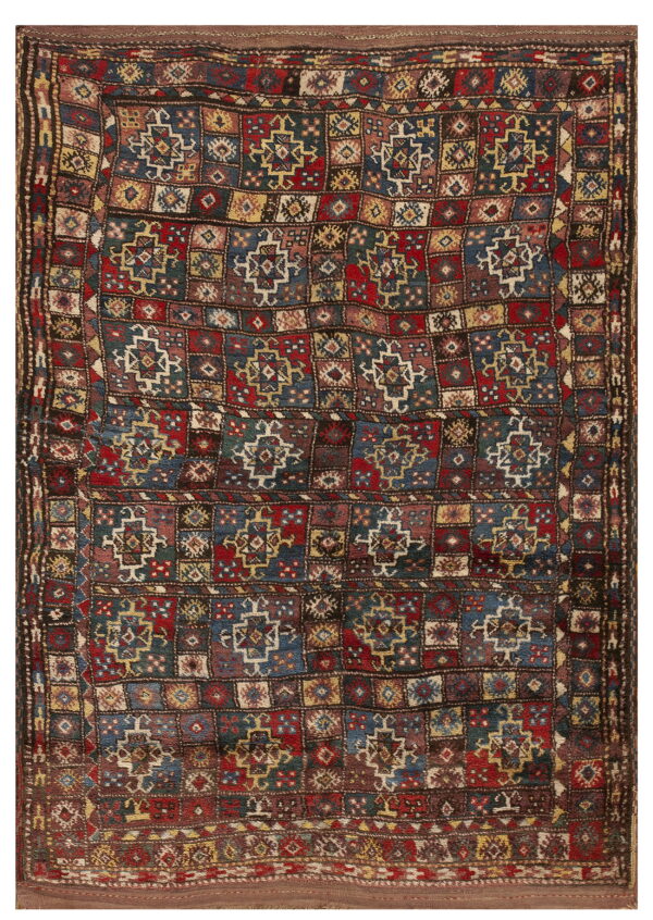 A richly colored rug with a geometric grid pattern using deep red, blue, yellow, and brown tones.