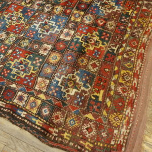 Geometric patterned rug with red, blue, and gold squares rests on rustic wood flooring.