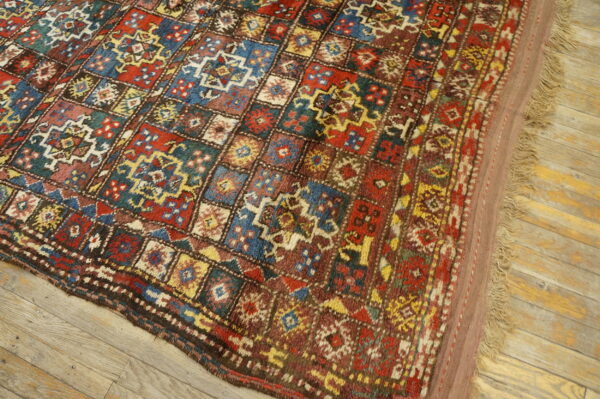 Geometric patterned rug with red, blue, and gold squares rests on rustic wood flooring.