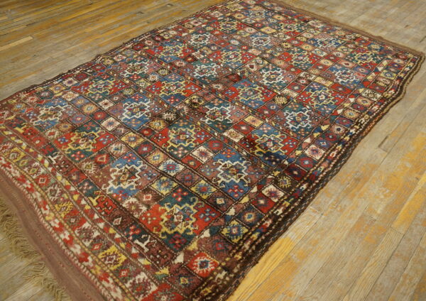Low-pile rug with a complex, colorful diamond pattern in red, blue, and brown rests on distressed light hardwood.