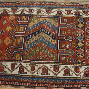 Red and blue tribal-style rug with complex geometric motifs on a weathered wood floor.