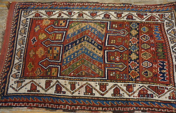 Red and blue tribal-style rug with complex geometric motifs on a weathered wood floor.