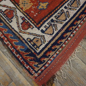 Close-up of a rustic rug corner with red, blue, and tan geometric patterns on distressed wood flooring.
