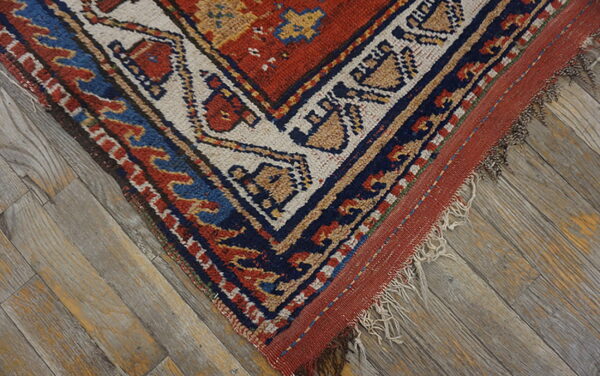 Close-up of a rustic rug corner with red, blue, and tan geometric patterns on distressed wood flooring.