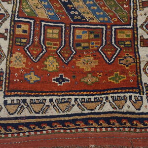 Geometric tribal rug detail showing a rust-red field and complex borders on light wood flooring.