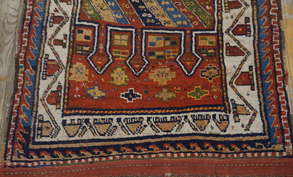 Geometric tribal rug detail showing a rust-red field and complex borders on light wood flooring.