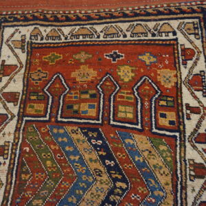 Colorful tribal rug with a red field, geometric arch motifs, and striped sections over distressed wood flooring.