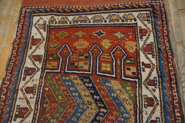 Colorful tribal rug with a red field, geometric arch motifs, and striped sections over distressed wood flooring.