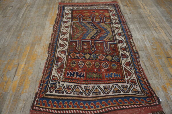 Red, blue, and ivory geometric pattern rug with low pile lies on distressed wooden floorboards.