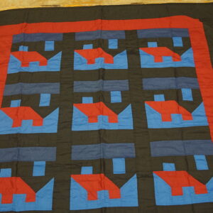 Red and blue geometric house patterns repeat on a dark cloth rug lying on yellow wood planks.