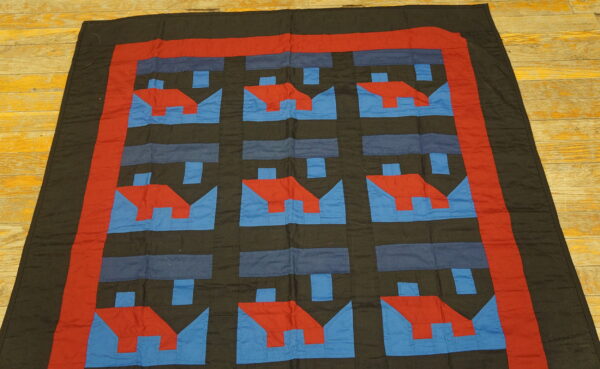 Red and blue geometric house patterns repeat on a dark cloth rug lying on yellow wood planks.