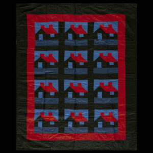 Black quilted textile featuring a repeating pattern of red-roofed houses against blue and black squares.
