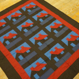 Red, blue, and dark brown flat textile with a bold geometric grid pattern resting on bright wood floors.