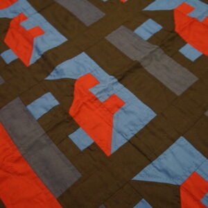 A flat textile with stitched geometric blocks in brown, bright orange, light blue, and slate gray.