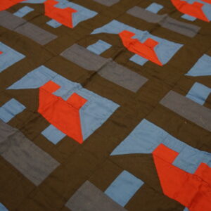 Flat geometric textile in dark brown, slate, red-orange, and light blue patchwork with visible stitching.
