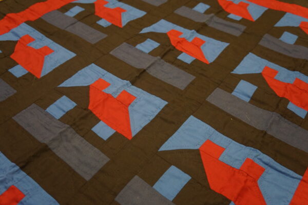 Flat geometric textile in dark brown, slate, red-orange, and light blue patchwork with visible stitching.