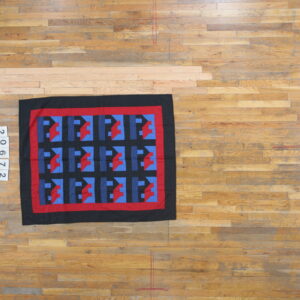 Geometric rug in black, red, and two shades of blue rests on light brown wooden floorboards.