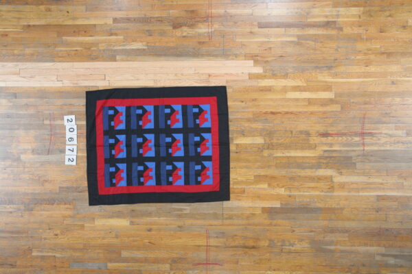 Geometric rug in black, red, and two shades of blue rests on light brown wooden floorboards.