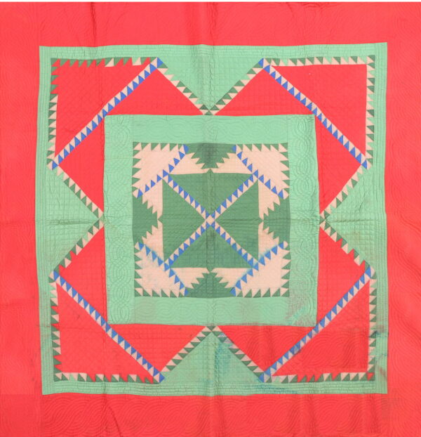 A vibrant textile rug with concentric geometric borders and sawtooth designs in coral red and shades of green.