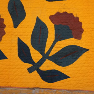 Mustard yellow quilted textile featuring dark teal and maroon floral motifs on weathered wood planks.