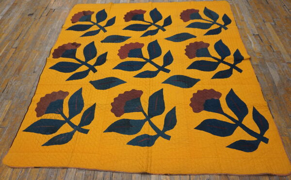 Yellow flatweave rug with repeating dark teal and maroon botanical patterns on rustic wood planks.