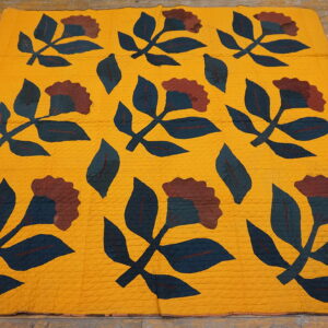 Yellow textile rug featuring dark blue and maroon floral appliqué patterns on wooden floorboards.