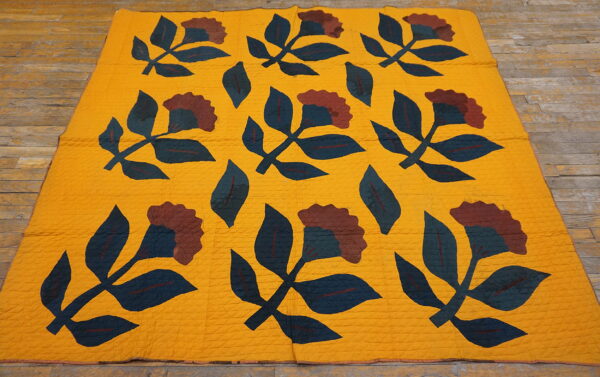Yellow textile rug featuring dark blue and maroon floral appliqué patterns on wooden floorboards.