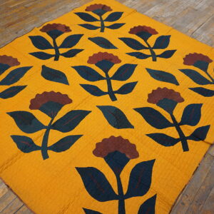 A flat, textured yellow textile with large maroon and dark blue floral motifs covers distressed wood planks.